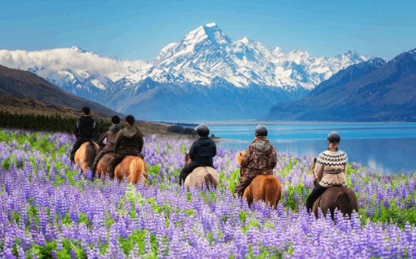 People horseback riding near mountains and lake.