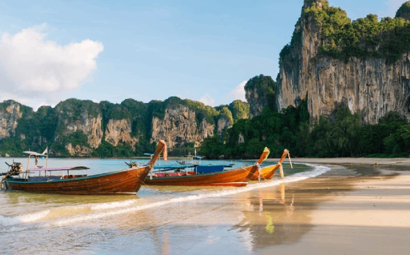Boats on a tropical beach with cliffs.