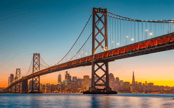 Bridge with city skyline at sunset.